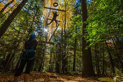 Landmark College student ascends ropes challenge course with spotter watching on.